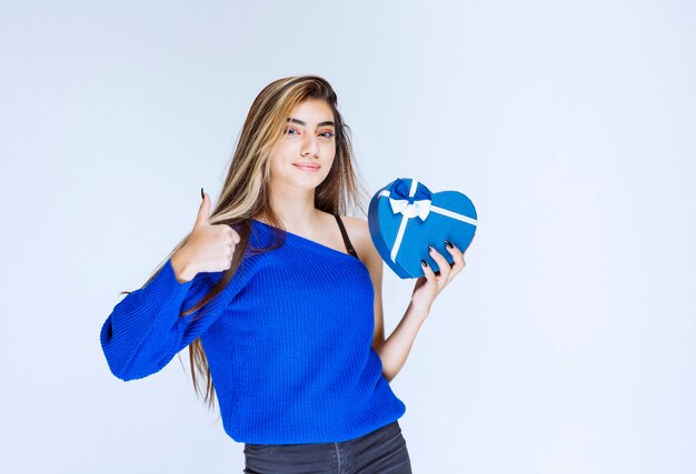 Meisje met een blauwe hartvormige geschenkdoos die zich positief en tevreden voelt.