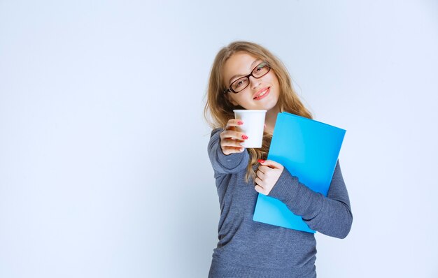 Meisje met een blauwe map die een kopje koffie aanbiedt aan haar collega.