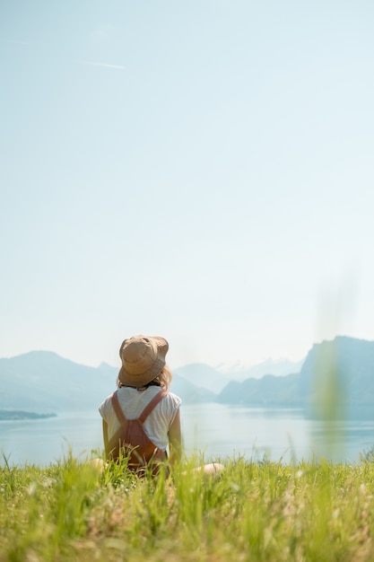 Meisje met een hoed zittend op een groen gazon in de buurt van het meer