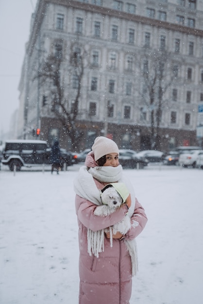 Meisje met een hond in haar armen op een straat in de stad sneeuw valt snow