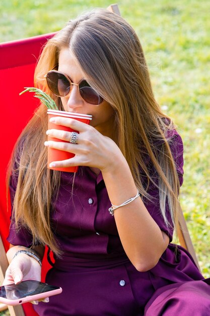 meisje met een smartphone en een cocktail op de natuur in een ligstoel. Zomerse vrije dag.