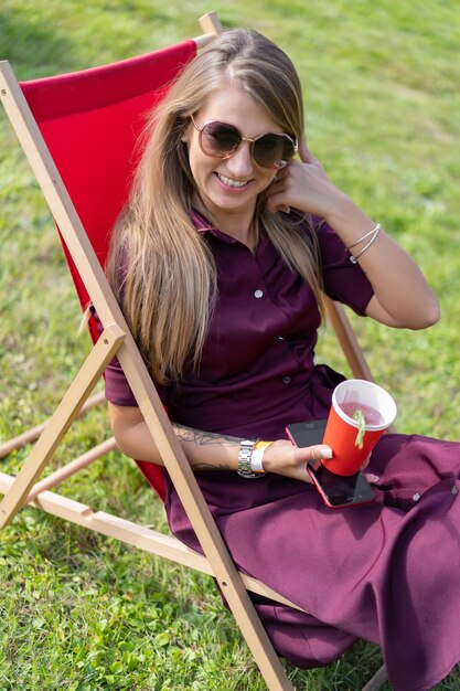 meisje met een smartphone en een cocktail op de natuur in een ligstoel. Zomerse vrije dag.