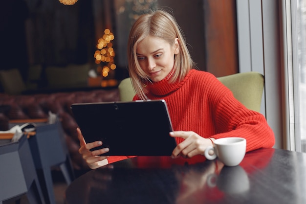 Meisje met een tablet. Vrouw in een café. Dame zit aan de tafel.