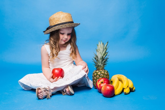 Meisje met fruit dat op blauwe muur wordt geïsoleerd