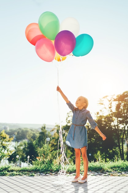 Meisje met kleurrijke ballonnen die zich uitstrekt tot de hemel en dromen