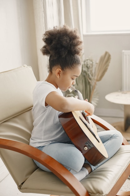 Meisje met krullend haar. gitaar leren spelen. klein meisje in een stoel.