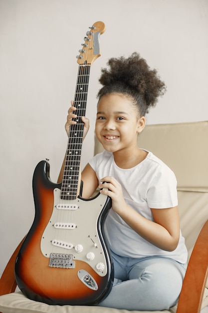 Meisje met krullend haar. Gitaar leren spelen. Klein meisje in een stoel.