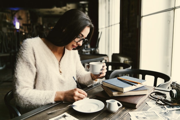 Gratis foto meisje met lang haar drinkt koffie aan de tafel in café en maakt enkele aantekeningen