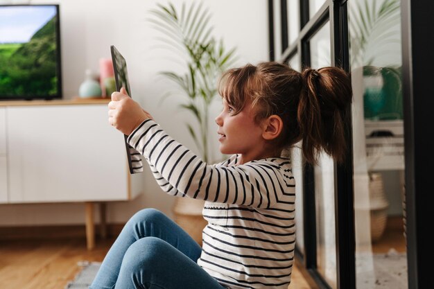Meisje met paardenstaart neemt selfie in woonkamer en houdt tablet vast