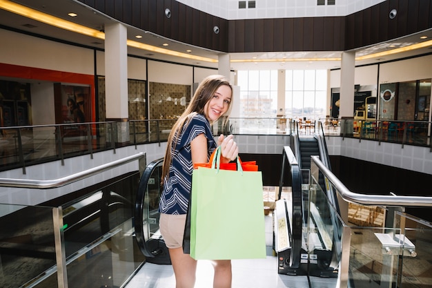 Meisje met papieren tassen gebaren in winkelcentrum