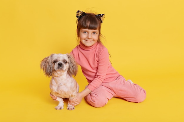 Meisje met puppy die binnen stellen en op geel glimlachen