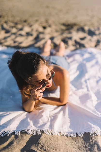 Meisje met zonnebril liggend op een handdoek op het strand