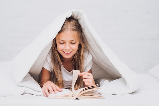 Meisje onder de deken die een boek leest