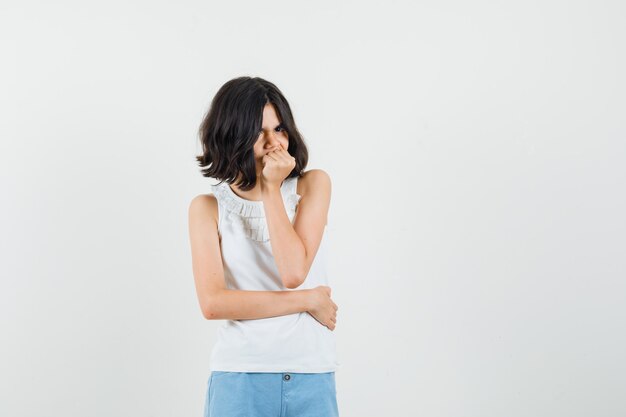 Meisje permanent in denken pose in witte blouse, korte broek en op zoek somber, vooraanzicht.