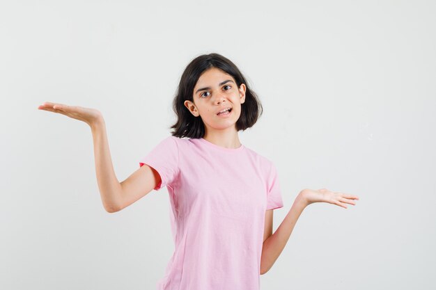 Meisje schalen gebaar maken in roze t-shirt en op zoek verward. vooraanzicht.