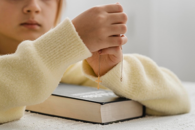 Meisje thuis bidden met bijbel en kruis ketting