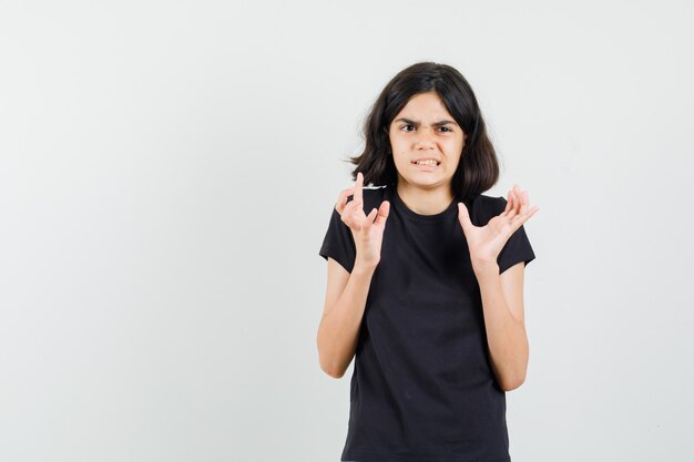 Meisje verhogen handen in zwart t-shirt en op zoek bang, vooraanzicht.