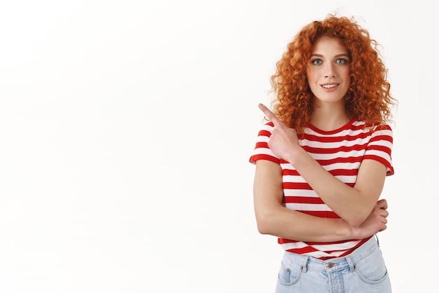 Meisje vraagt vriend of ze al geweldige promo zag Attactive roodharige krullende vrouw wijzend linker bovenhoek wijsvinger glimlachend ontspannen blik nieuwsgierig vrolijk camera staande witte achtergrond