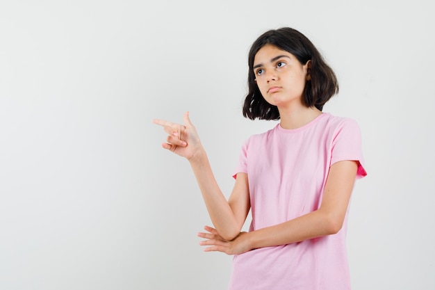 Meisje wijst naar de zijkant in roze t-shirt en kijkt peinzend. vooraanzicht.