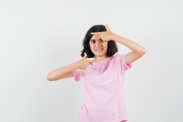 Meisje wijst naar de zijkant in roze t-shirt en ziet er vrolijk uit. vooraanzicht.