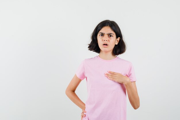 Meisje wijst naar zichzelf in roze t-shirt en kijkt verbaasd. vooraanzicht.