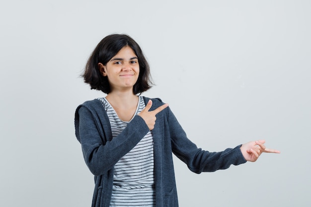 Meisje wijst opzij in t-shirt, jasje en kijkt vrolijk.