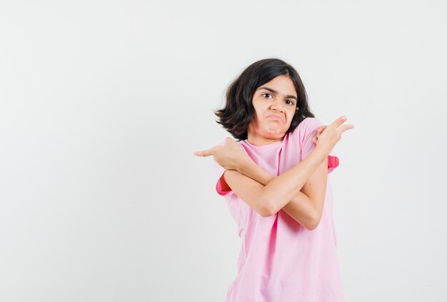 Meisje wijst weg in roze t-shirt en kijkt verward. vooraanzicht.