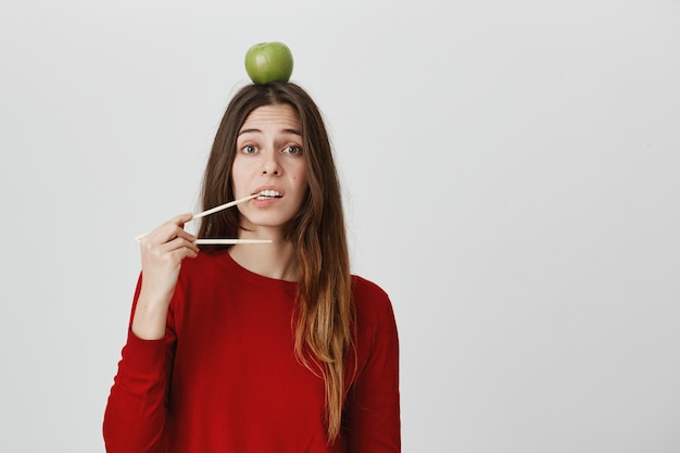 Meisje wil eten, eetstokjes bijten, groene appel op het hoofd houden