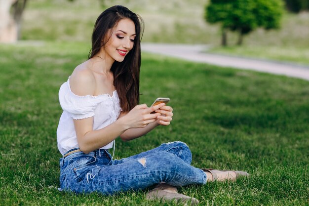 Meisje zit in een park te typen op haar mobiele telefoon