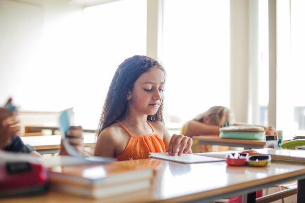 Gratis foto meisje zitten op school bureau bladeren