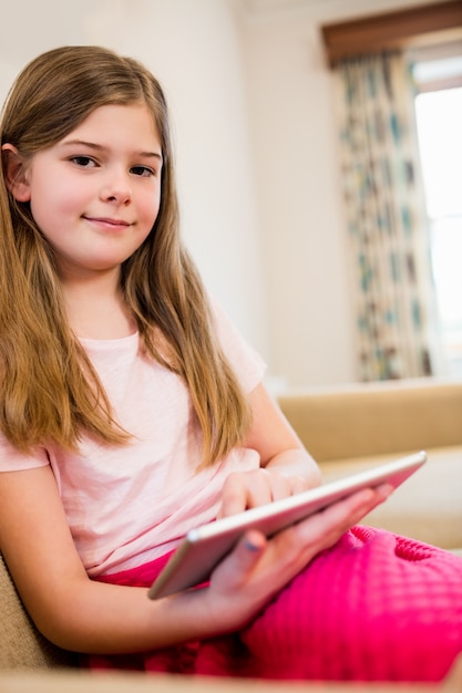 Meisje zittend op de bank met behulp van digitale tablet in woonkamer