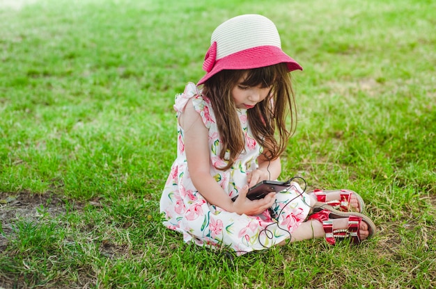 Meisje, zittend op het gras te kijken naar een mobiele telefoon met een koptelefoon