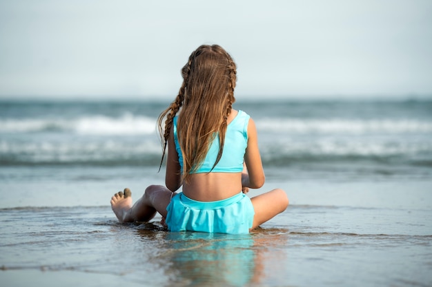 Meisje zittend op het strand achteraanzicht