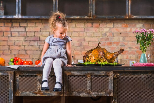 Meisje, zittend op tafel met gebakken kalkoen