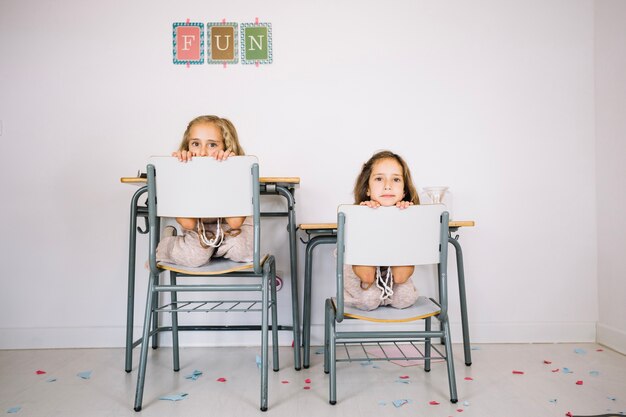 Meisjes die achter achterruggen van stoelen gluren