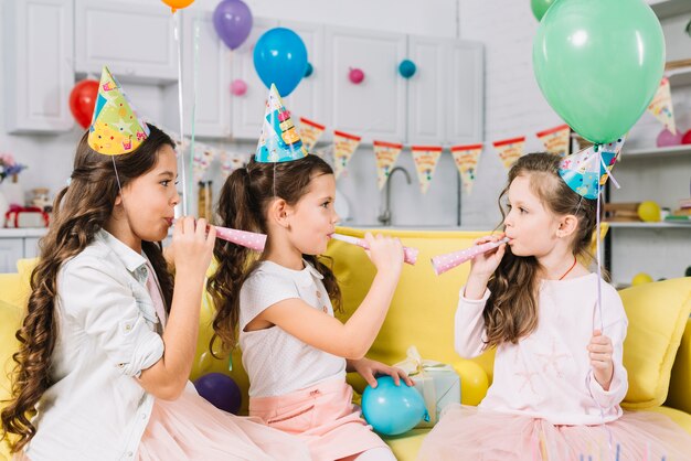 Meisjes die ballons houden en partijhoorn blazen tijdens verjaardag