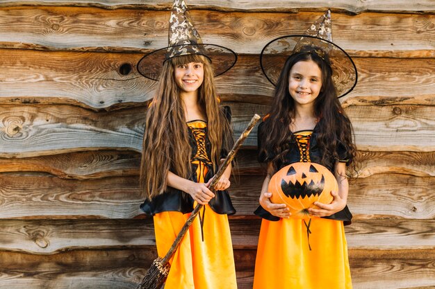 Meisjes in Halloween-kostuums met bezem en pompoen die camera bekijken