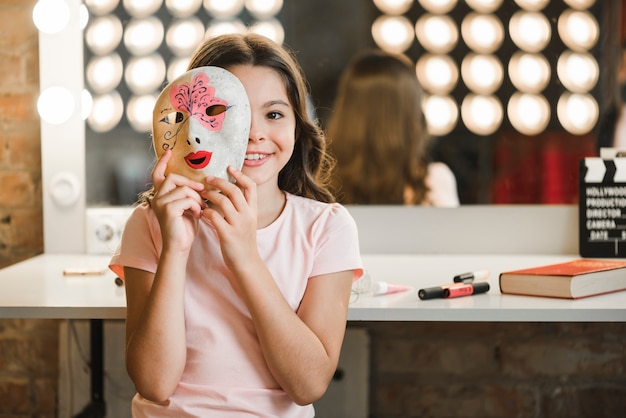 Meisjeszitting bij backstage die Venetiaans masker voor haar gezicht houden