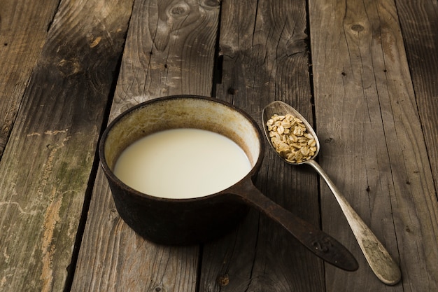 Melk in de oude pan en lepel haver op de rustieke houten achtergrond