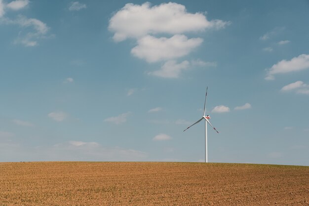 Mening van windturbine en bruin landbouwbedrijf onder de blauwe hemel en witte wolken