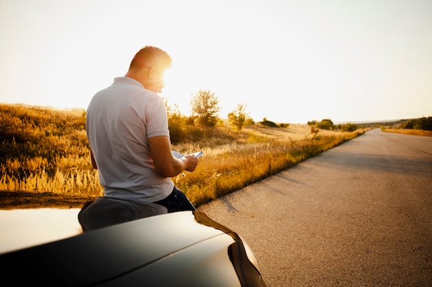 Mens die een boekzitting op de autokap leest