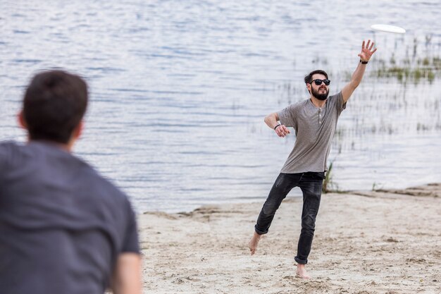 Mens die frisbee vangen die van vriend op strand vliegen