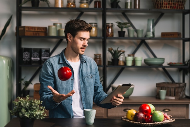 Mens die fruit in lucht werpt die digitale tablet bekijkt