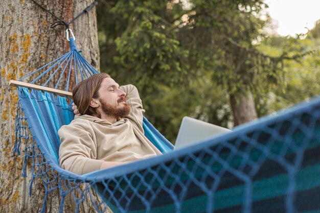 Mens die in hangmat van aard met laptop geniet