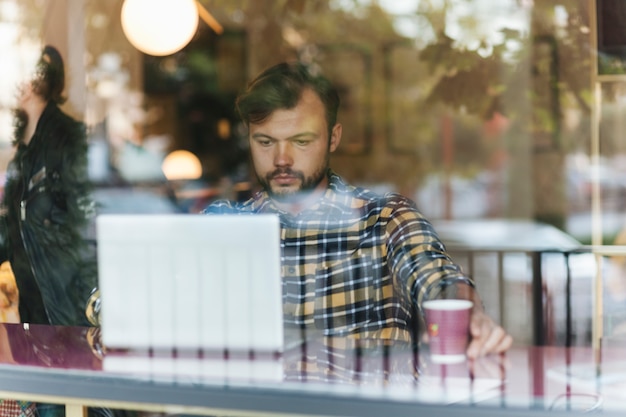 Gratis foto mens die laptop in koffiewinkel met behulp van