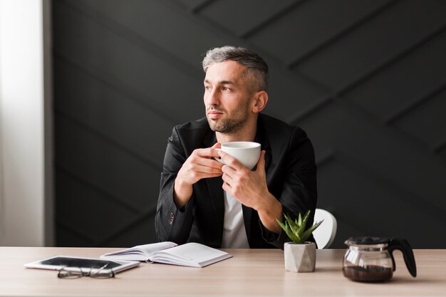 Mens die met zwart jasje zijdelings zittend zijn bureau bekijkt