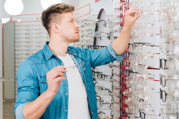 Gratis foto mens die nieuwe glazen zoekt bij optometrist