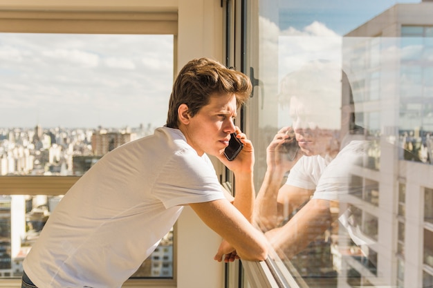 Mens die op mobiele telefoon spreekt die door glasvenster kijkt