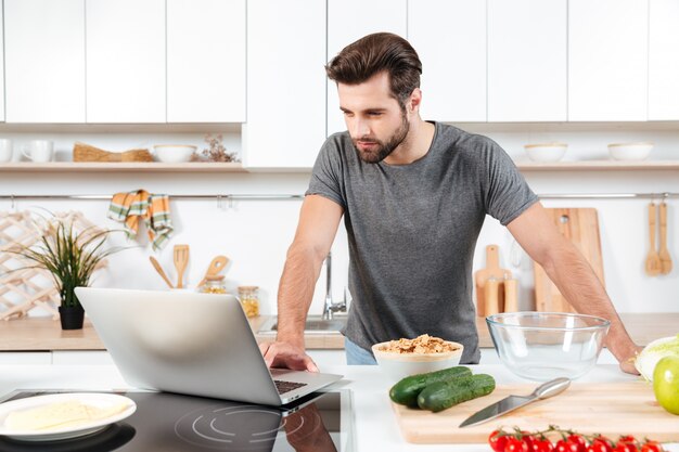 Mens die recept thuis op laptop in keuken kijken