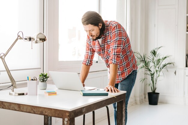 Mens die zich dichtbij de lijst bevindt die laptop bekijkt